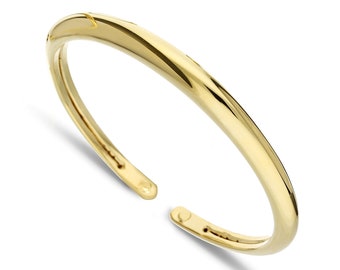Puede incluir: Un brazalete simple de oro con una superficie lisa y redondeada. El brazalete está abierto y tiene un cierre con bisagra.
