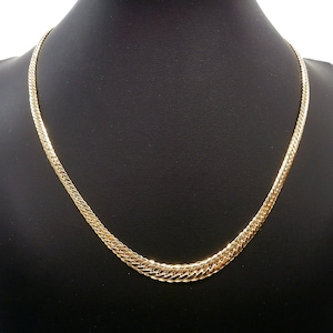 May include: A gold chain necklace with a flat, textured design. The chain is on a black display stand.