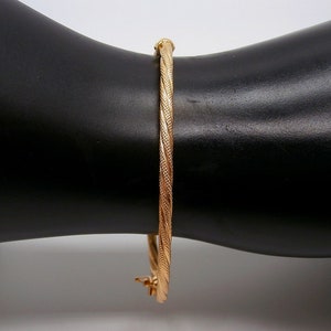 May include: A gold bangle bracelet with a twisted design. The bracelet is on a black surface.