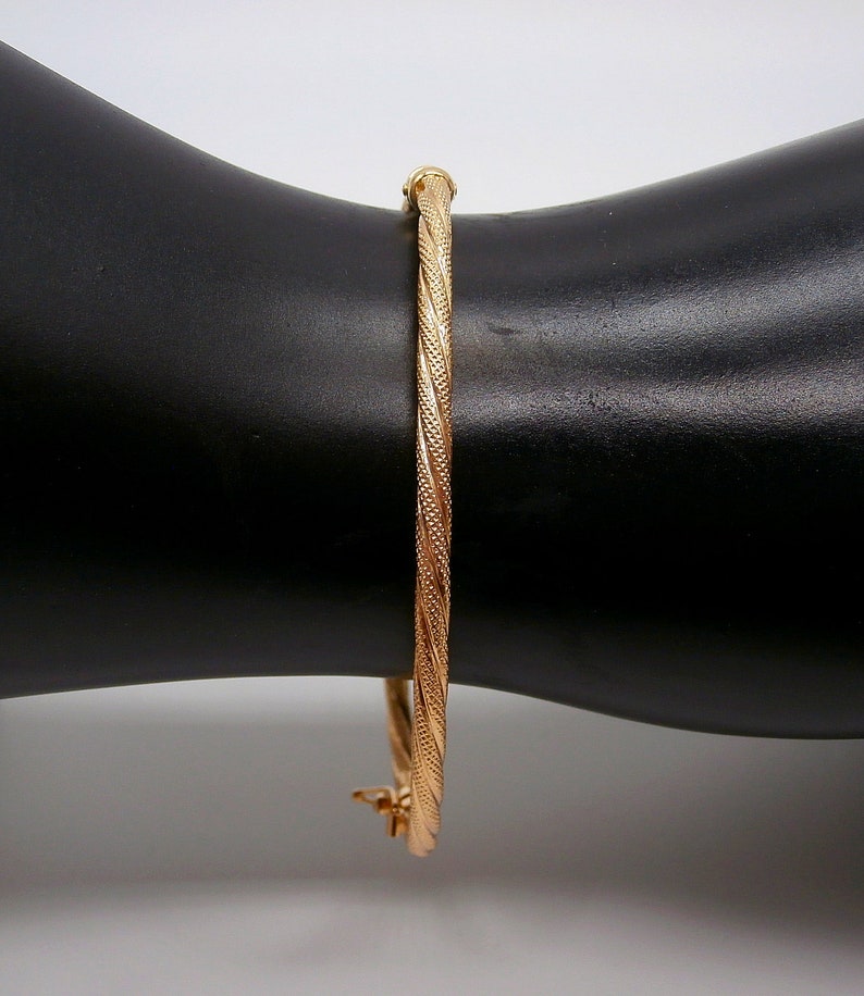 May include: A gold bangle bracelet with a twisted design. The bracelet is on a black surface.