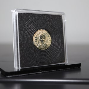 Peut inclure: Une pi&egrave;ce de monnaie romaine en argent avec un portrait d'un homme sur un c&ocirc;t&eacute; et du texte sur l'autre. La pi&egrave;ce est pr&eacute;sent&eacute;e dans un bo&icirc;tier en plastique transparent avec un fond noir.