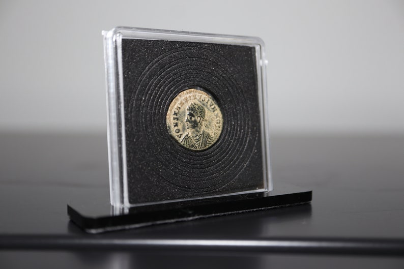 Peut inclure: Une pi&egrave;ce de monnaie romaine en argent avec un portrait d'un homme sur un c&ocirc;t&eacute; et du texte sur l'autre. La pi&egrave;ce est pr&eacute;sent&eacute;e dans un bo&icirc;tier en plastique transparent avec un fond noir.
