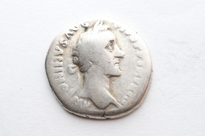 May include: Silver Roman coin with a portrait of a man on one side and Latin text on the other.
