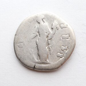 May include: Silver coin with a portrait of a person standing and holding a branch with leaves. The coin has a raised rim and a smooth surface. The coin has the letter "D" on the left side.