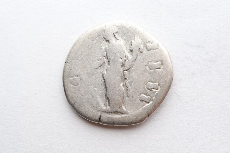 May include: Silver coin with a portrait of a person standing and holding a branch with leaves. The coin has a raised rim and a smooth surface. The coin has the letter "D" on the left side.