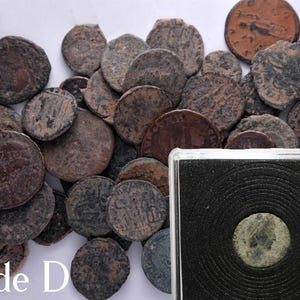 Peut inclure: Une collection de pi&egrave;ces de monnaie en cuivre romaines anciennes dans diff&eacute;rents &eacute;tats d'usure. Les pi&egrave;ces sont dispos&eacute;es en pile sur une surface blanche. Les pi&egrave;ces sont de tailles et de formes diff&eacute;rentes, et certaines portent des inscriptions visibles. Le texte "Grade D" est visible dans le coin inf&eacute;rieur gauche de l'image.
