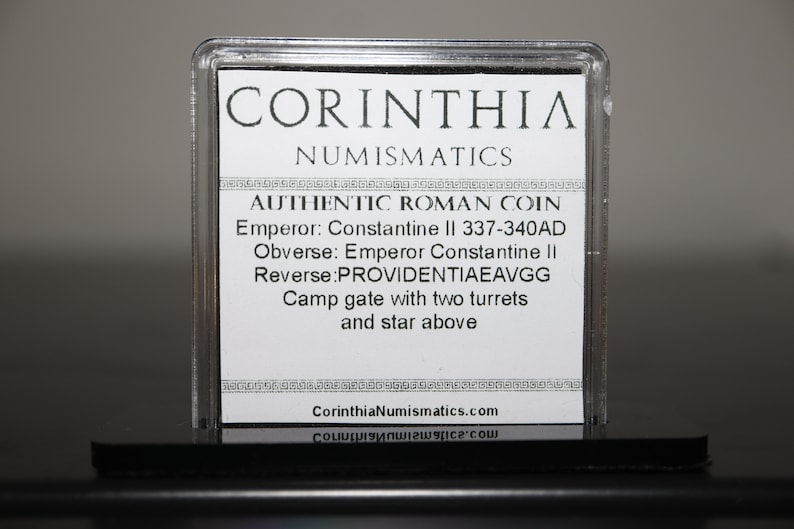 Peut inclure: Une carte blanche avec du texte noir dans un bo&icirc;tier en plastique transparent. Le texte indique "CORINTHIA NUMISMATICS AUTHENTIC ROMAN COIN Emperor: Constantine II 337-340AD Obverse: Emperor Constantine II Reverse: PROVIDENTIAEAVGG Camp gate with two turrets and star above CorinthiaNumismatics.com".