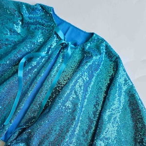 May include: A turquoise blue sequined cape with a satin ribbon tie and a pom-pom trim.