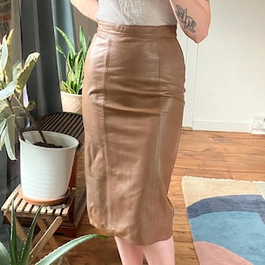 May include: A brown leather pencil skirt. The skirt is knee-length and has a fitted silhouette. The skirt is a medium brown color and appears to be made of genuine leather. The skirt is worn with a striped top.