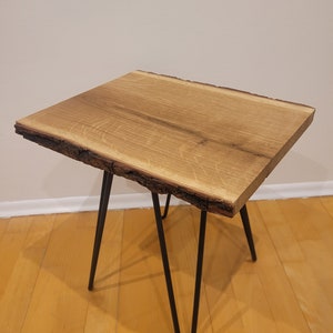 Könnte beinhalten: Ein kleiner Holz-Beistelltisch mit einer Tischplatte mit lebender Kante und schwarzen Haarnadelbeinen. Der Tisch ist aus Naturholz mit rustikalem Finish.