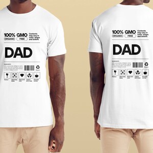 Peut inclure: T-shirt blanc avec du texte noir qui dit "100% GMO FREE ORGANIC" et "DAD". Le t-shirt a également une étiquette avec un code-barres et des icônes.