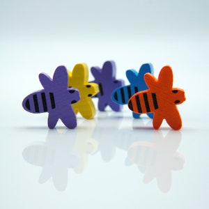 Può includere: Cinque figurine di api in legno in fila. Le api sono dipinte in diversi colori: viola, giallo, blu e arancione. Ogni ape ha strisce nere.