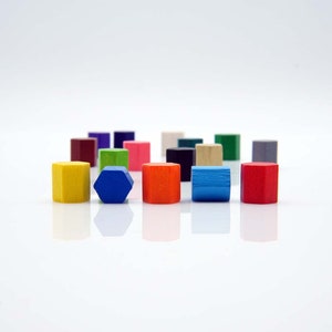 Puede incluir: Una colección de bloques de madera de colores en varias formas, incluyendo cuadrados, hexágonos y rectángulos. Los bloques están dispuestos en un semicírculo sobre una superficie blanca.