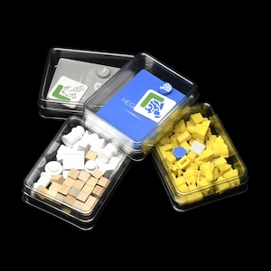May include: Four clear plastic containers holding game pieces. One container holds a blue card with the word "HEG" and a logo. Another contains yellow and blue blocks. The third has white and tan pieces. The fourth has a grey card.