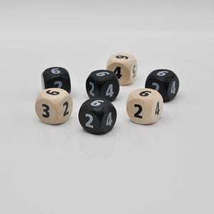 Pode incluir: Uma coleção de dados de madeira, alguns pretos e outros bege, com números brancos. Os dados são numerados de 2 a 6. Os dados estão dispostos sobre uma superfície branca.