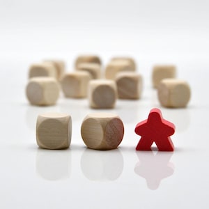 May include: A collection of small, light-coloured wooden cubes arranged in the background, with two wooden cubes and one red wooden human-shaped game piece positioned in the foreground. The objects have a smooth, natural finish and rounded edges.