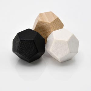 Pu&ograve; includere: Tre forme geometriche in legno di colore nero, bianco e legno naturale. Le forme sono tutte della stessa dimensione e hanno un design sfaccettato.