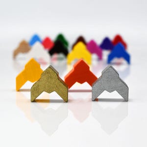 Può includere: Una collezione di colorati pezzi di legno per giochi a forma di cime montuose stilizzate. I pezzi sono in vari colori, tra cui giallo, oro, arancione e grigio, con altri sullo sfondo. I pezzi sono disposti su una superficie bianca.