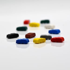 May include: A selection of small, brightly coloured wooden car toys. The cars are in various colours, including red, yellow, blue, and black. They are arranged on a white surface. These toys are ideal for children and are approximately 4 cm long.
