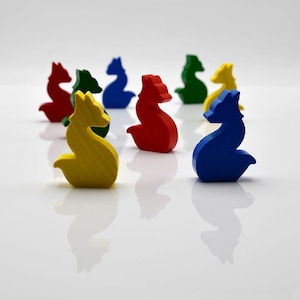 May include: A collection of colorful wooden fox figurines in red, green, blue, yellow, and other colors. The figurines are arranged on a white surface, with their reflections visible. The fox figures are likely game pieces or decorative items.