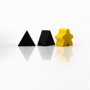 Puede incluir: Tres piezas de juego de madera sobre una superficie blanca. Dos piezas triangulares negras y una pieza amarilla con forma de persona están dispuestas en fila. Las piezas tienen un acabado brillante y proyectan reflejos.