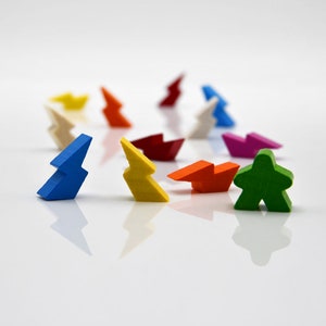 May include: A collection of colorful wooden game pieces, including lightning bolt shapes in blue, yellow, and orange, and a green person-shaped piece. The pieces are arranged on a white surface, suggesting a board game or educational toy.