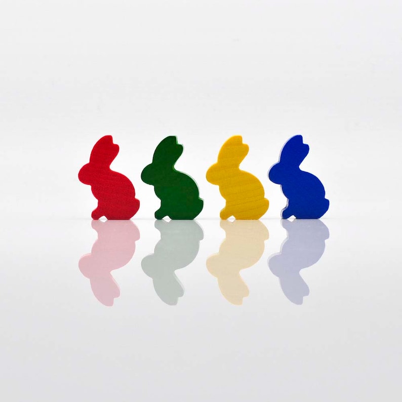 K&ouml;nnte beinhalten: Vier Holz-Hasenfiguren in einer Reihe aufgereiht. Die Hasen sind in verschiedenen Farben bemalt: rot, gr&uuml;n, gelb und blau.