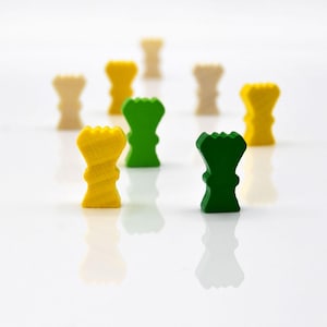 May include: A group of wooden game pieces in yellow and green. The pieces are shaped like crowns and are arranged in a semi-circle on a white surface.