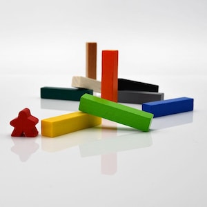 Könnte beinhalten: Eine Sammlung farbenfroher Holzspielsteine, darunter rechteckige Blöcke in Grün, Gelb, Blau, Orange und Grau sowie eine rote Figur. Die Teile sind auf einer weißen Oberfläche angeordnet, was auf ein Brettspiel oder ein Lernspielzeug hindeutet.
