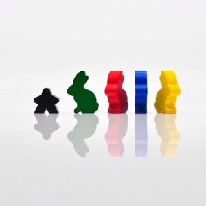 K&ouml;nnte beinhalten: F&uuml;nf h&ouml;lzerne Spielfiguren, darunter ein schwarzer Bauer und vier Hasenfiguren in Gr&uuml;n, Rot, Blau und Gelb.