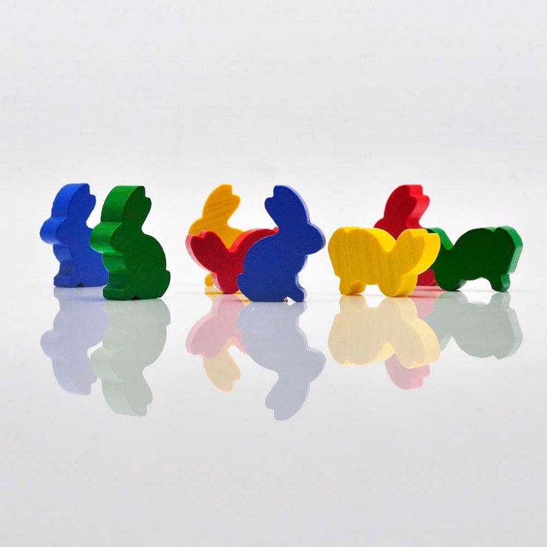K&ouml;nnte beinhalten: Ein Set aus sieben Holz-Hasenfiguren in verschiedenen Farben, darunter Blau, Gr&uuml;n, Rot und Gelb. Die Hasen sind alle in die gleiche Richtung ausgerichtet und in einer Reihe angeordnet.