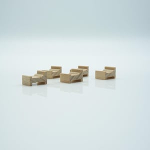 May include: Six small, unfinished wooden bed miniatures. Each bed has a headboard and footboard, with a simple, stepped design. The beds are arranged on a white surface, suggesting a craft or model-making theme.