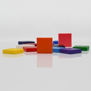 May include: A collection of colourful wooden squares in various shades of red, blue, green, yellow, and orange. The squares are arranged in a staggered pattern on a white surface.