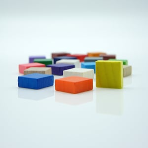 Könnte beinhalten: Eine Gruppe bunter Holzwürfel in verschiedenen Farbtönen von Blau, Grün, Rot, Gelb, Weiß und Braun. Die Würfel sind in einem Halbkreis angeordnet, mit einem einzelnen gelben Würfel vorne.