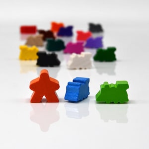 May include: A collection of colorful wooden game pieces, including orange people-shaped figures and blue and green train-shaped pieces. Other pieces in the background are red, brown, black, yellow, purple, pink, and white. The pieces are on a white surface.