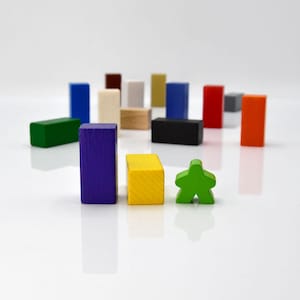 May include: A collection of colorful wooden blocks in various shapes and sizes, including a green block shaped like a person. The blocks are arranged in a row on a white surface.