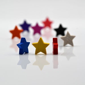Può includere: Un gruppo di stelle ornamentali in legno colorate in varie tonalità di blu, rosso, giallo, verde e bianco. Le stelle sono disposte a semicerchio su una superficie bianca.