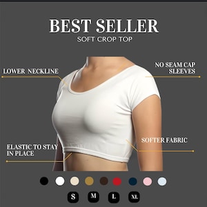 Könnte beinhalten: Weißes Crop-Top mit kurzen Ärmeln und einem tieferen Ausschnitt. Das Oberteil ist aus weichem Stoff gefertigt und hat ein elastisches Band am Saum, um es an Ort und Stelle zu halten. Der Text "BEST SELLER" und "SOFT CROP TOP" befindet sich oben im Bild. Der Text "NO SEAM CAP SLEEVES" befindet sich rechts im Bild. Der Text "LOWER NECKLINE" befindet sich links im Bild. Der Text "SOFTER FABRIC" befindet sich rechts im Bild. Der Text "ELASTIC TO STAY IN PLACE" befindet sich links im Bild. Der Text "S, M, L, XL" befindet sich unten im Bild.