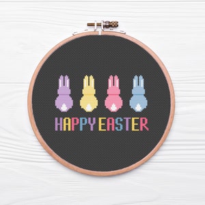 May include: A black embroidery hoop with a cross-stitch design of four colorful bunnies and the text "HAPPY EASTER".