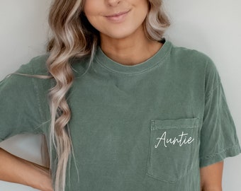 May include: A green t-shirt with a pocket that says "Auntie" in white cursive lettering.
