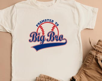 Könnte beinhalten: Ein cremefarbenes T-Shirt mit dem Text "Promoted to Big Bro" in Rot und Blau, mit einer Baseball-Grafik. Kombiniert mit einer braunen Hose. Ein lässiges Outfit für ein junges Kind.