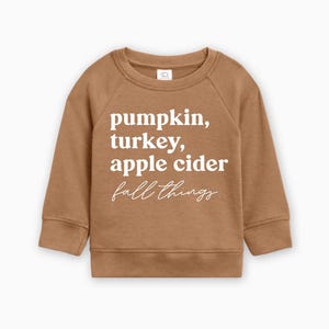 May include: A brown sweatshirt with the text "pumpkin, turkey, apple cider fall things" printed in white.