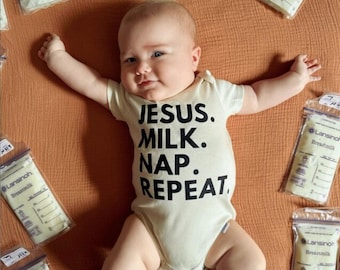 May include: A baby wearing a cream-colored onesie with the words "JESUS. MILK. NAP. REPEAT." in black. The baby is surrounded by bags of breast milk on an orange-brown surface.