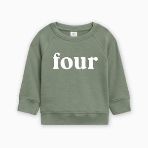 May include: Sage green sweatshirt with the word "four" printed in white across the front. The long-sleeved top has a crew neck and ribbed cuffs and hem. The sweatshirt is designed for children.