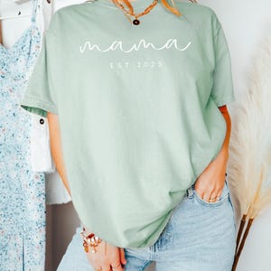 May include: A light green t-shirt with the text "mama est 2025" in white lettering.