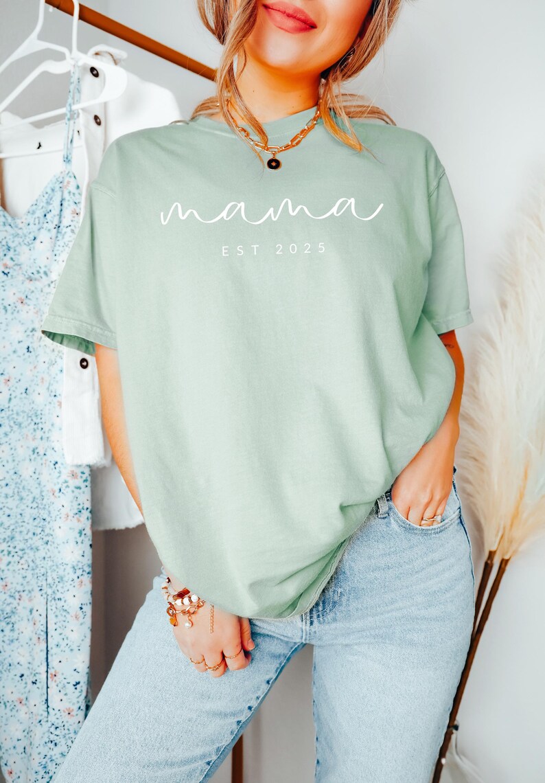 May include: A light green t-shirt with the text "mama est 2025" in white lettering.