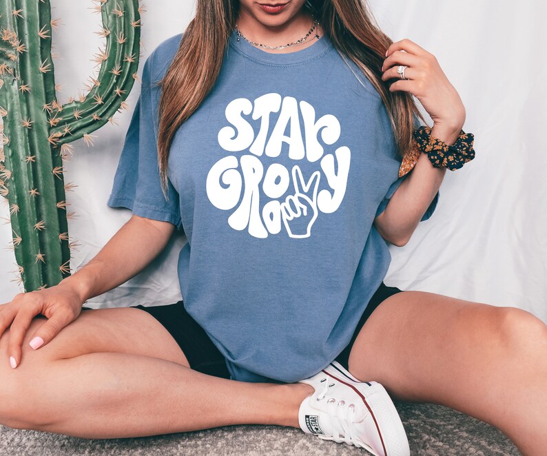 May include: A blue t-shirt with a white graphic that says "Stay Groovy" in a retro font with a peace sign.