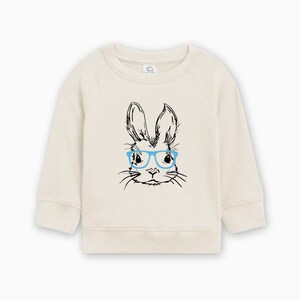 May include: A cream colored sweatshirt with a black and white illustration of a bunny wearing blue glasses.
