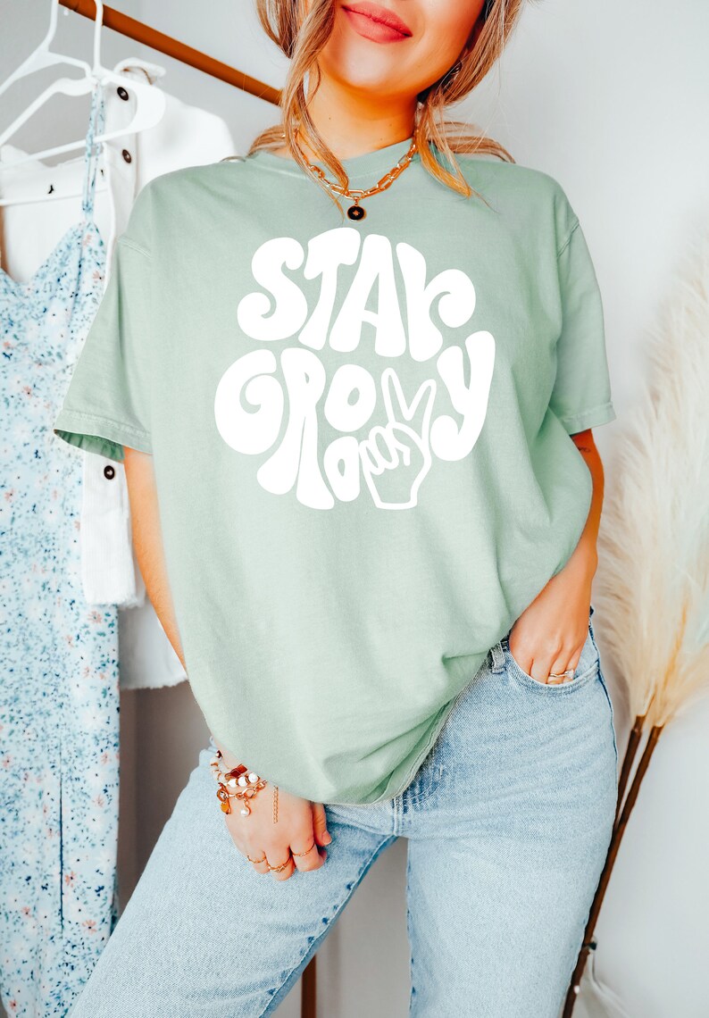 May include: A light green t-shirt with a white graphic that says "Stay Groovy" in a retro font with a peace sign.