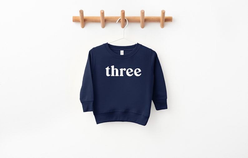 Puede incluir: Una sudadera de manga larga azul marino con la palabra "three" impresa en blanco en la parte delantera.